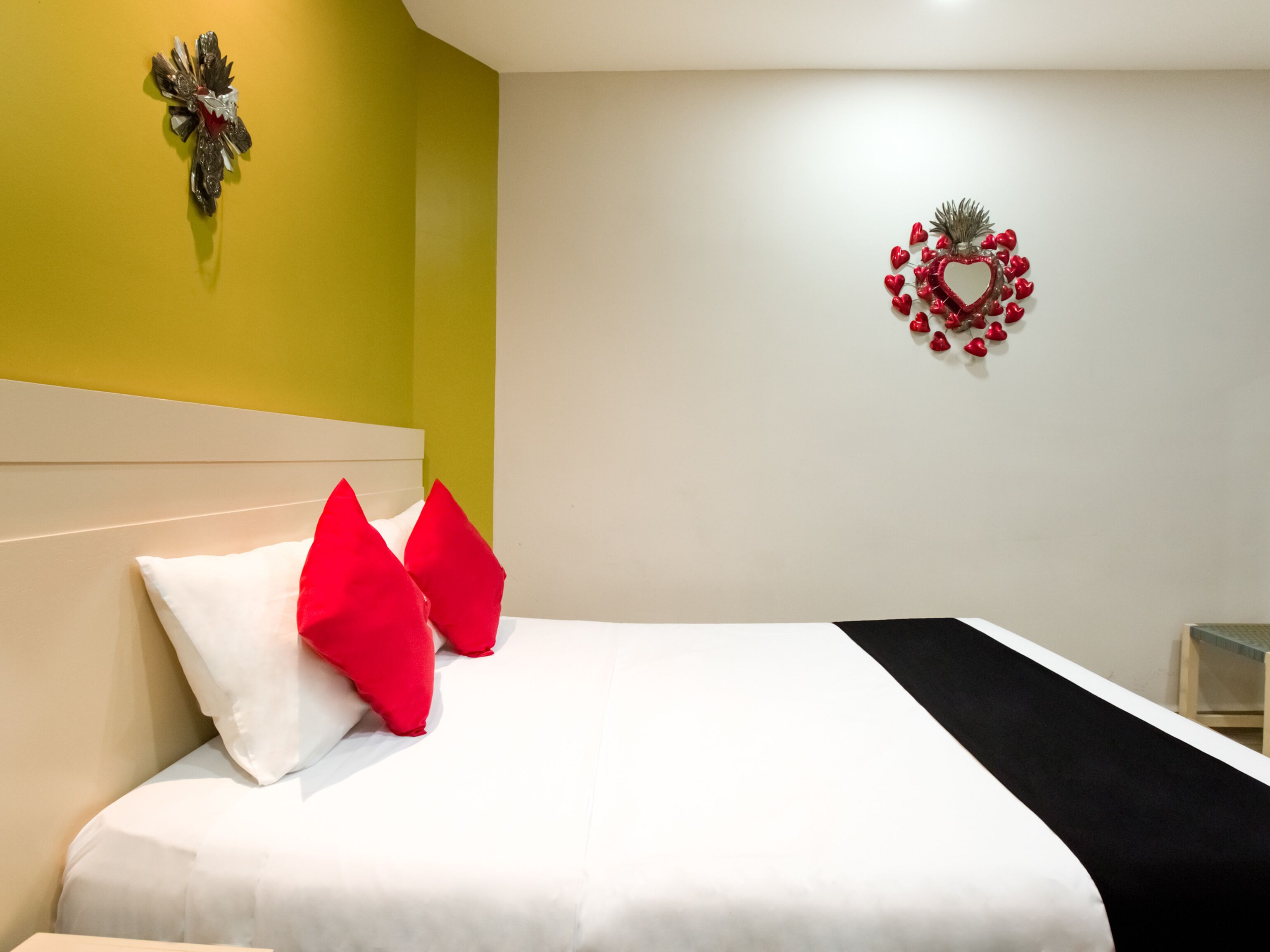 A bed with white and red pillows, a white headboard, and a black throw blanket.