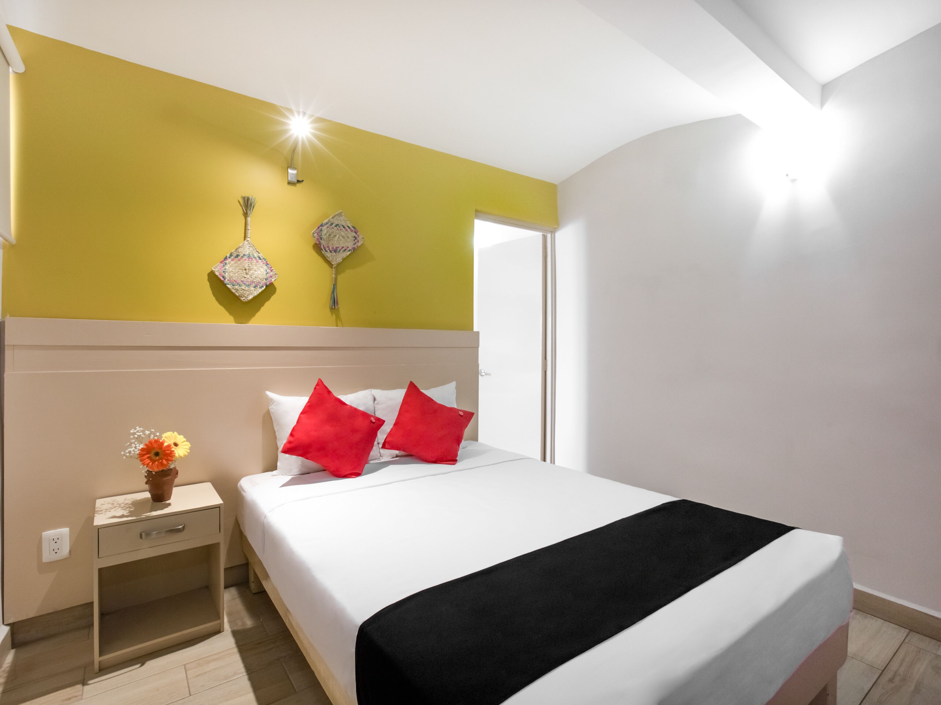Habitación de hotel con cama, mesita de noche, un jarrón con flores y adornos en la pared.
