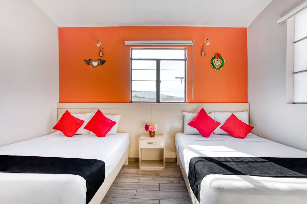 A hotel room with two beds, a window, and orange walls.