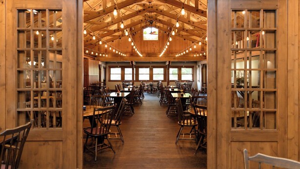 A spacious dining hall with wooden tables and chairs, large windows, and a high ceiling with exposed beams and hanging lights. - Brown County Inn (Nashville)