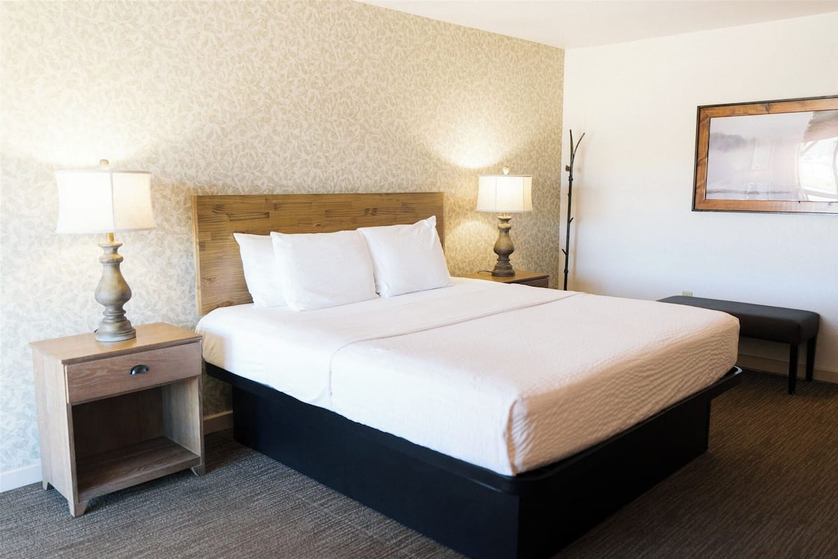 A hotel room with a bed, two bedside tables with lamps, a bench, and a framed picture on the wall.