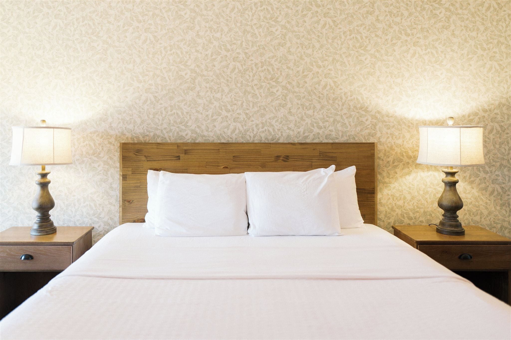 Un lit bien fait, avec du linge de lit blanc, deux lampes de chevet et une tête de lit en bois.