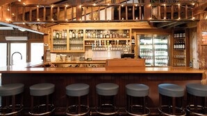 A bar area with wooden bar stools, a counter with a cash register, and shelves stocked with bottles and glasses. - Brown County Inn (Nashville)