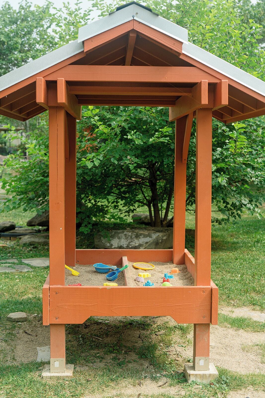 A wooden play structure with a roof, surrounded by a grassy area and trees.