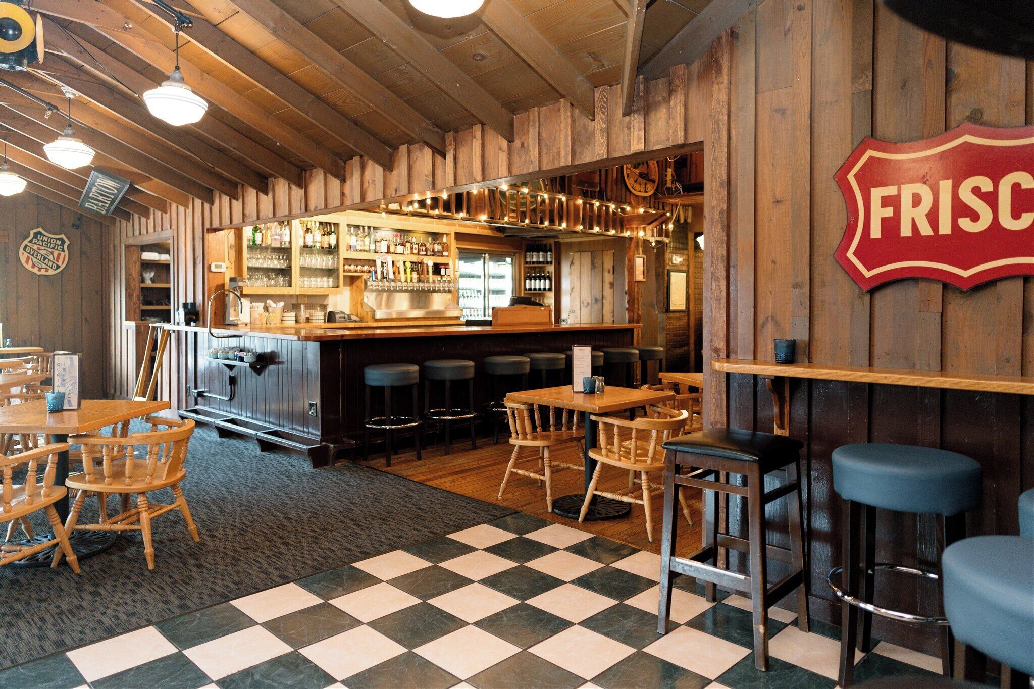 A bar area with wooden walls, a checkered floor, and bar stools.