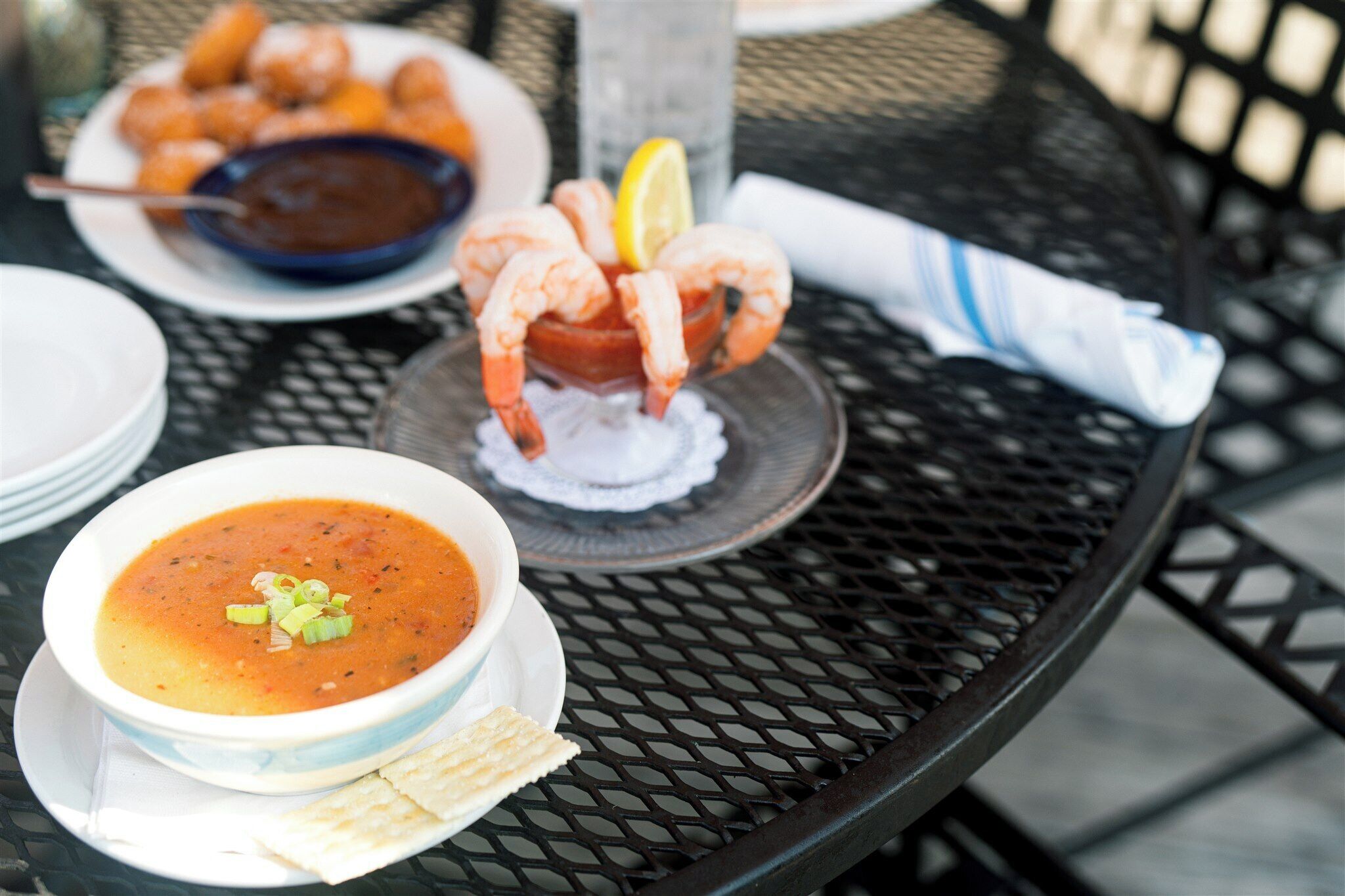 A table with a bowl of soup, a plate of shrimp, and a bowl of sauce.