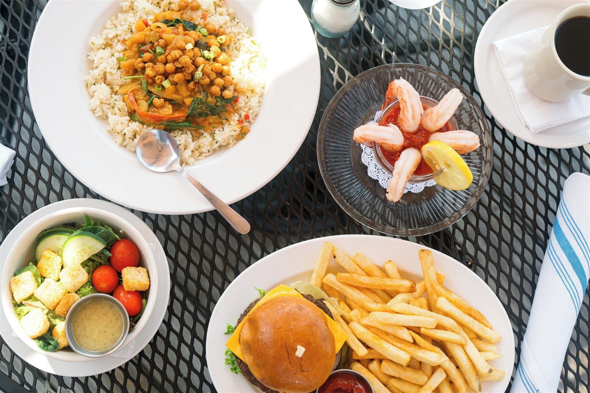 A table with various dishes including rice, shrimp, a burger, fries, and a salad.