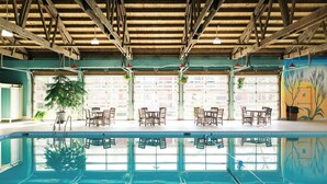 An indoor swimming pool with wooden beams, potted plants, and tables and chairs. - Brown County Inn (Nashville)