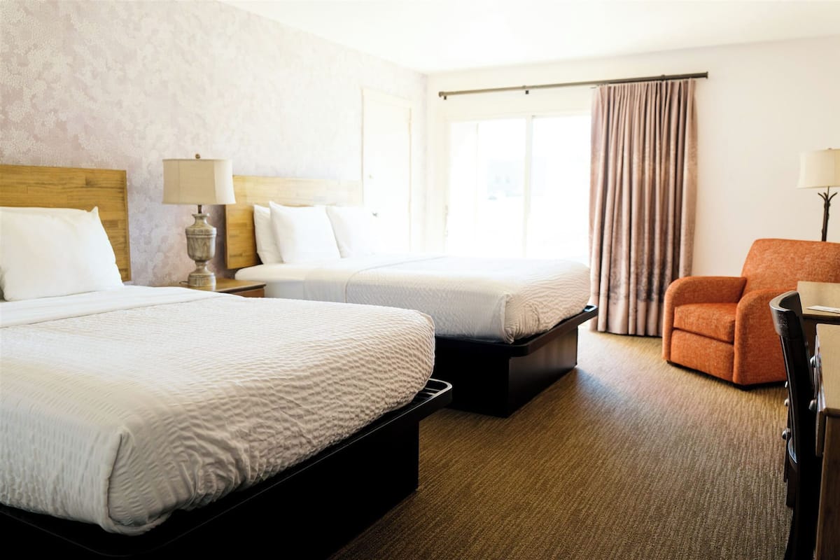 A hotel room with two beds, a desk, a chair, and a window with curtains.