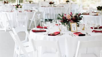 Un espacio para eventos al aire libre con carpas, mesas redondas, sillas blancas y centros de mesa florales.