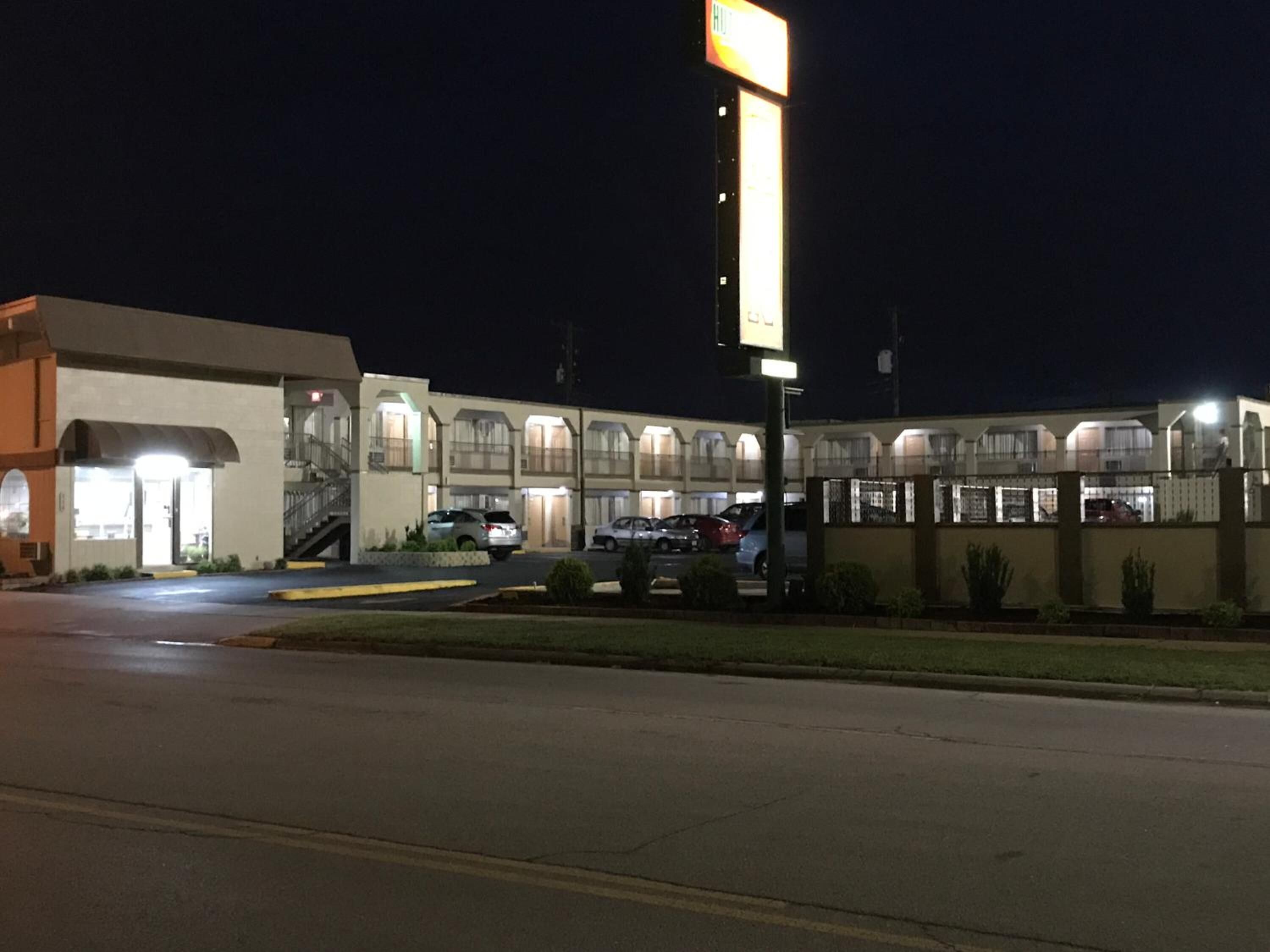 Un motel con entrada central, varios espacios de estacionamiento y un letrero iluminado.