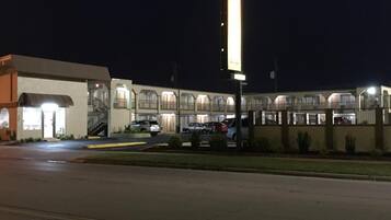 Un motel con entrada central, varios espacios de estacionamiento y un letrero iluminado.