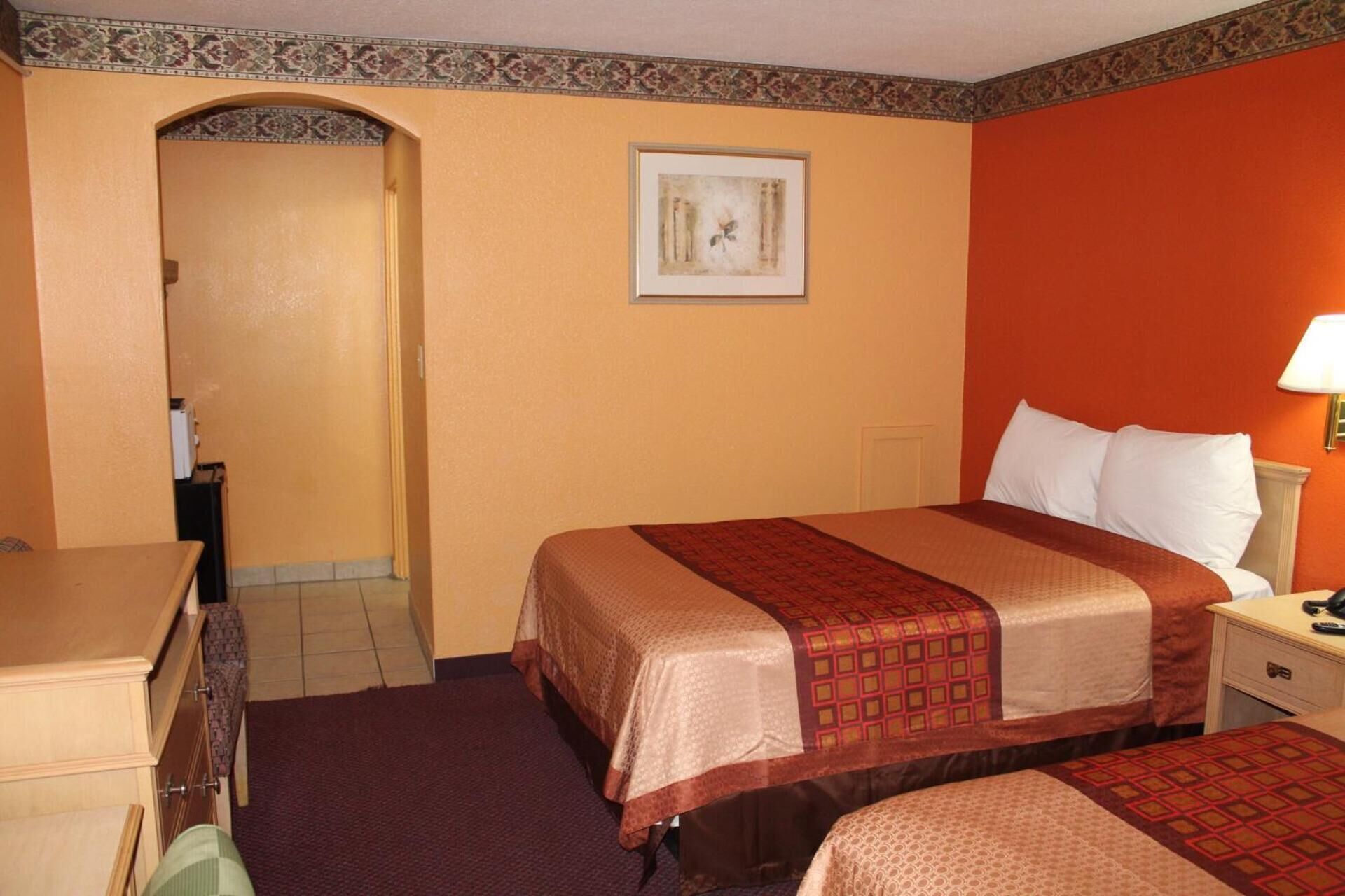 A hotel room with two beds, a desk, a chair, a nightstand, a lamp, and a framed picture on the wall.