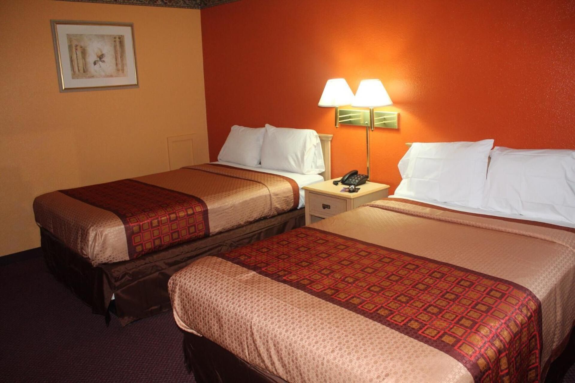 A hotel room with two beds, each with a patterned bedspread, a nightstand with a lamp, and a framed picture on the wall.