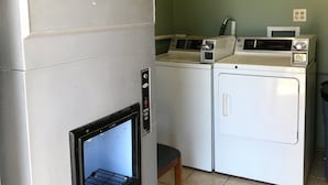 A laundry room with a front-loading washer and dryer, a microwave, and a small stool. - Hutchinson Inn (Hutchinson)