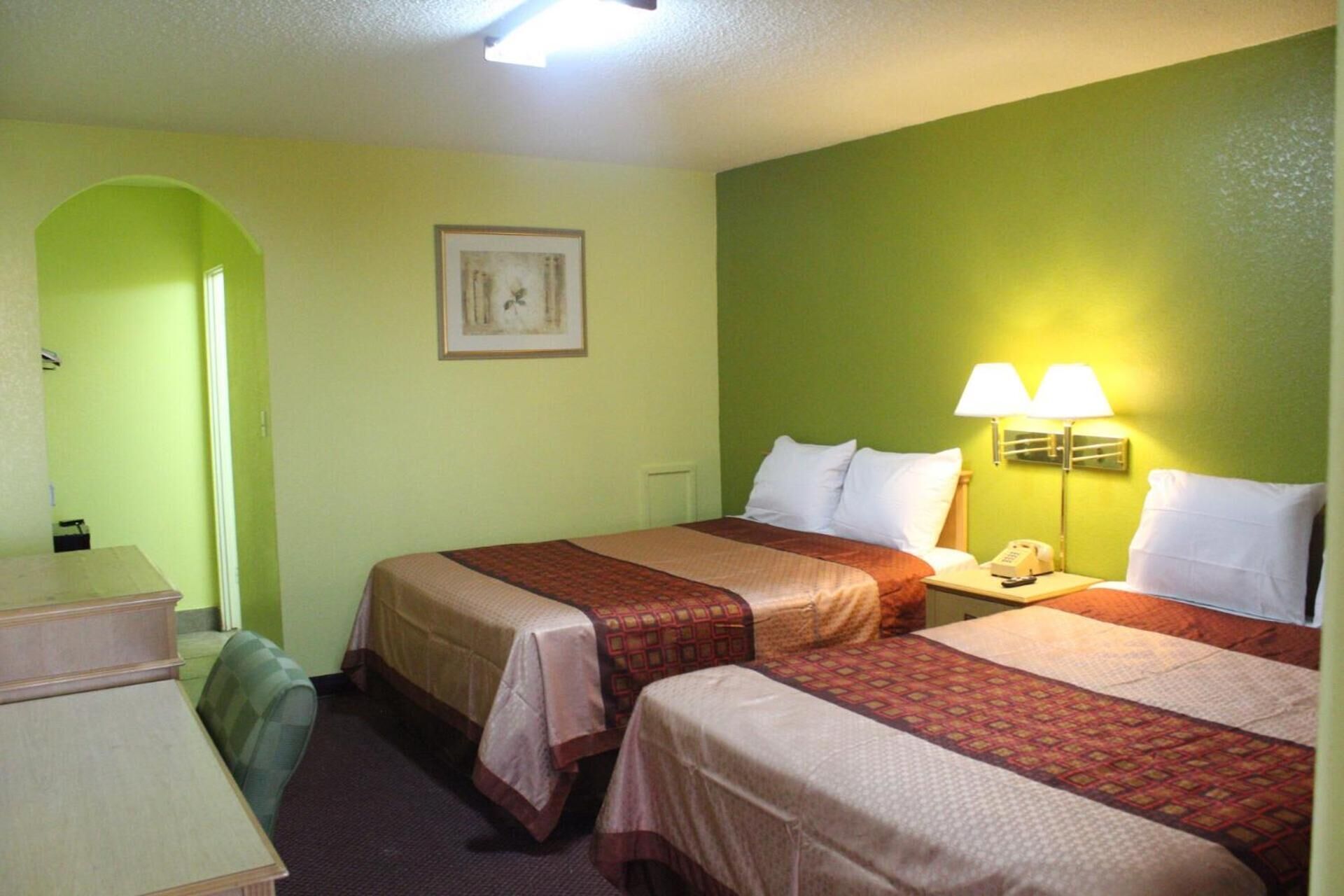 Habitación de hotel con dos camas, un escritorio y una silla. Se observa un cuadro en la pared y una lámpara en la mesita de noche.