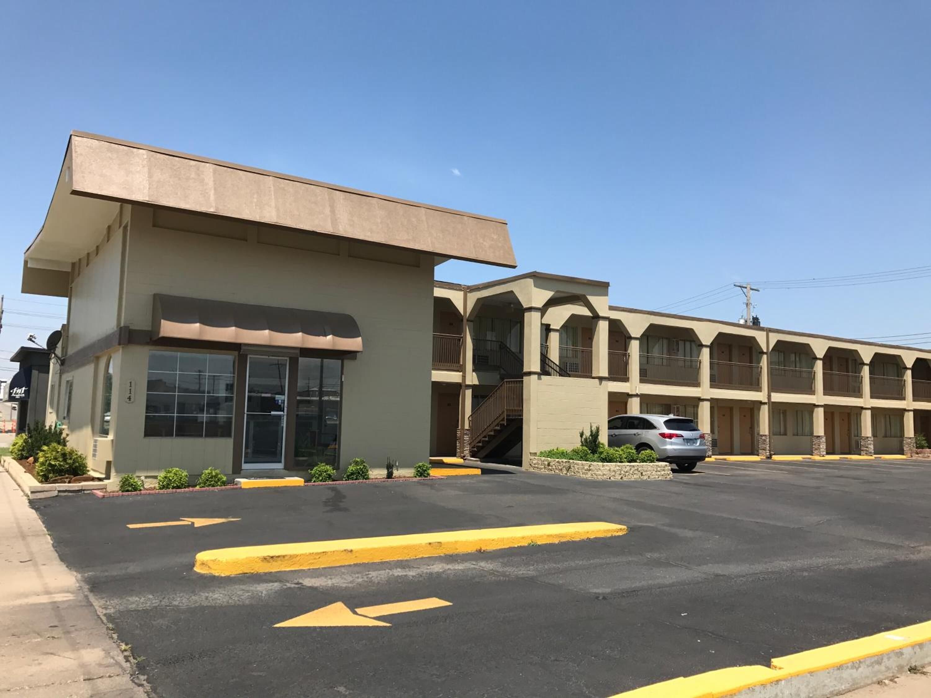 Un motel de una sola planta, con una pequeña entrada y un estacionamiento con flechas direccionales.
