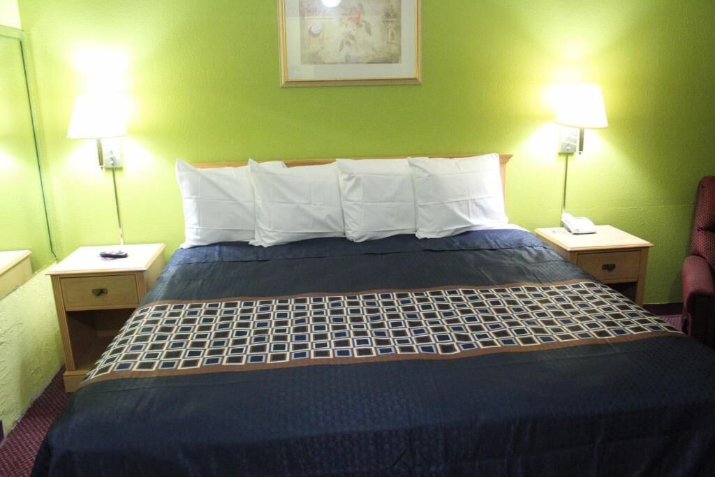 A hotel room with a bed, two bedside tables, a lamp, a chair, and a painting on the wall.