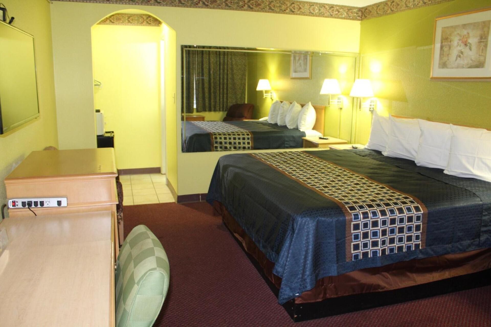 A hotel room with a bed, bedside lamps, a mirror, a desk, and a chair.