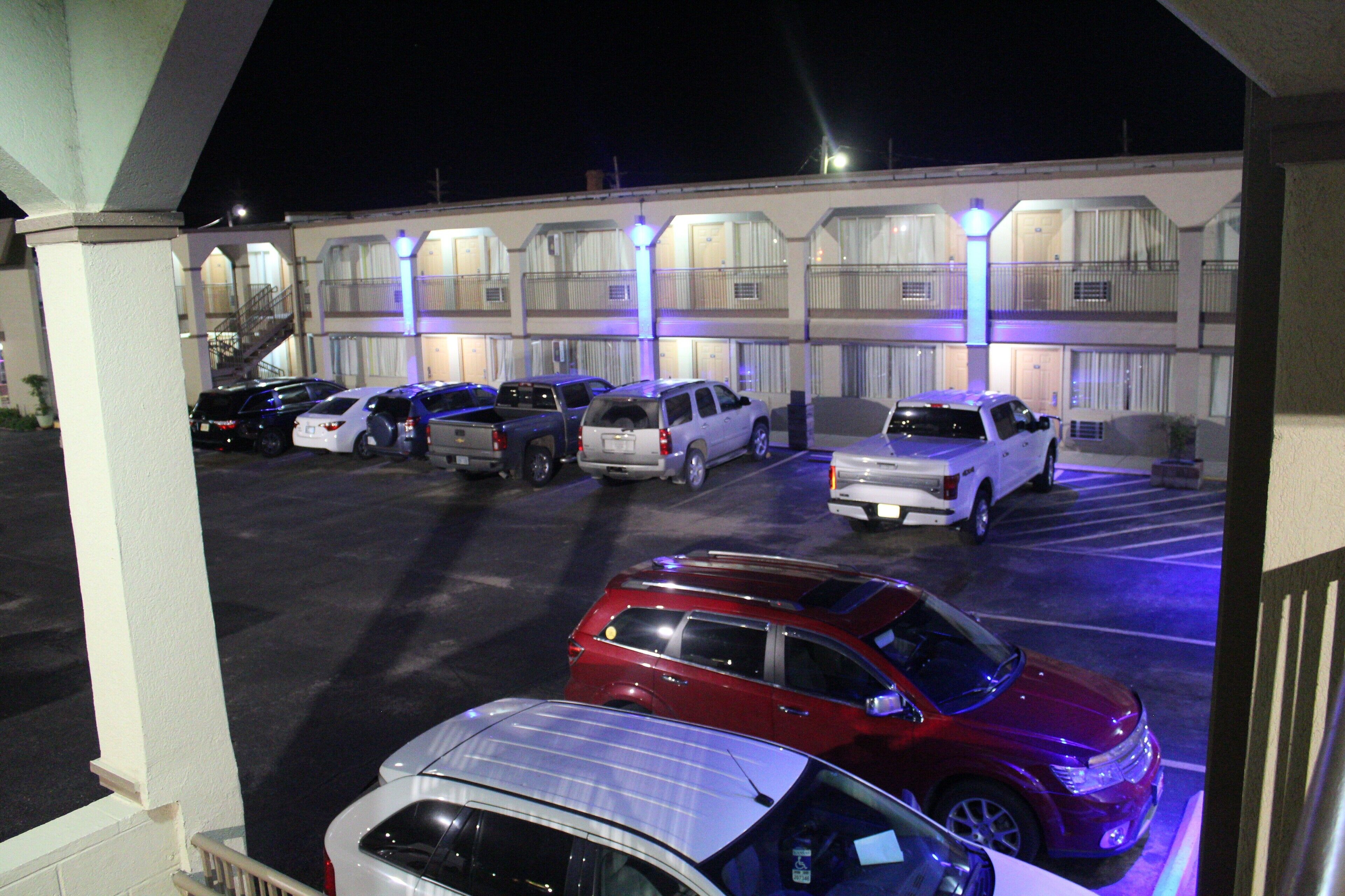 Um estacionamento com vários carros estacionados em frente a um motel com várias varandas e uma escadaria que leva à entrada.
