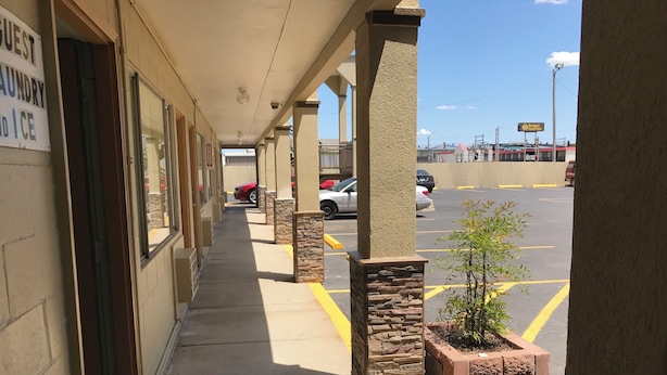 A covered walkway with a sign for guest laundry and ice, leading to a parking lot with cars and a small tree planter. - Hutchinson Inn (Hutchinson)