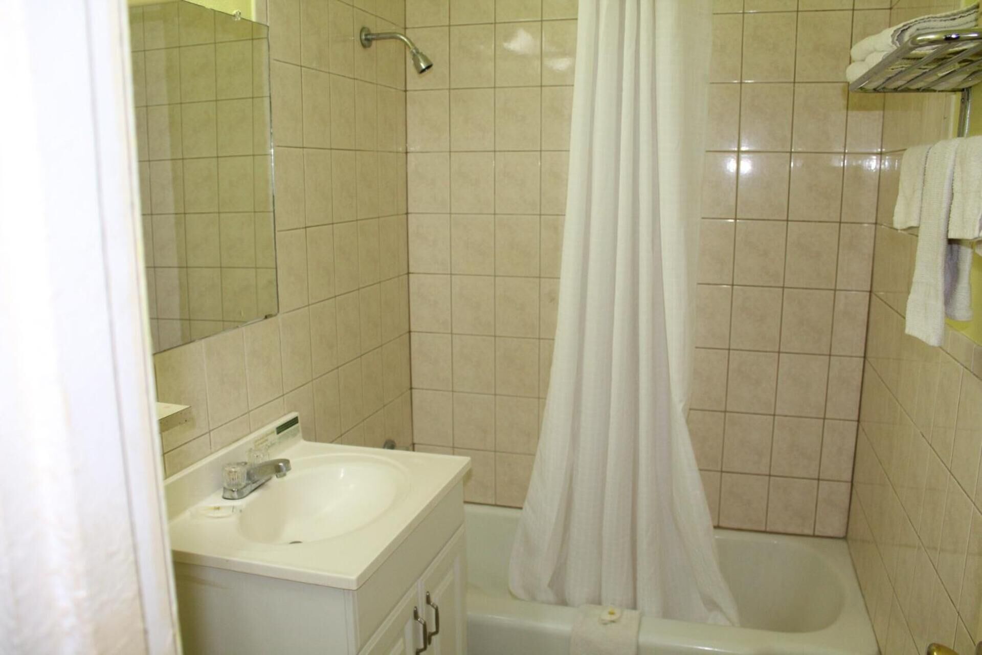 A bathroom with a sink, mirror, shower curtain, and bathtub.