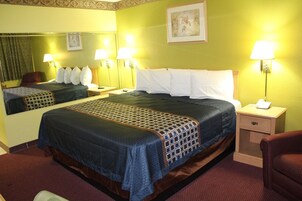 Una habitación de hotel con una cama grande, dos mesitas de noche, una silla y un espejo.