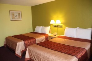 Two single beds with patterned bedspreads and pillows, a nightstand with a lamp, and a framed picture adorn this cozy space.