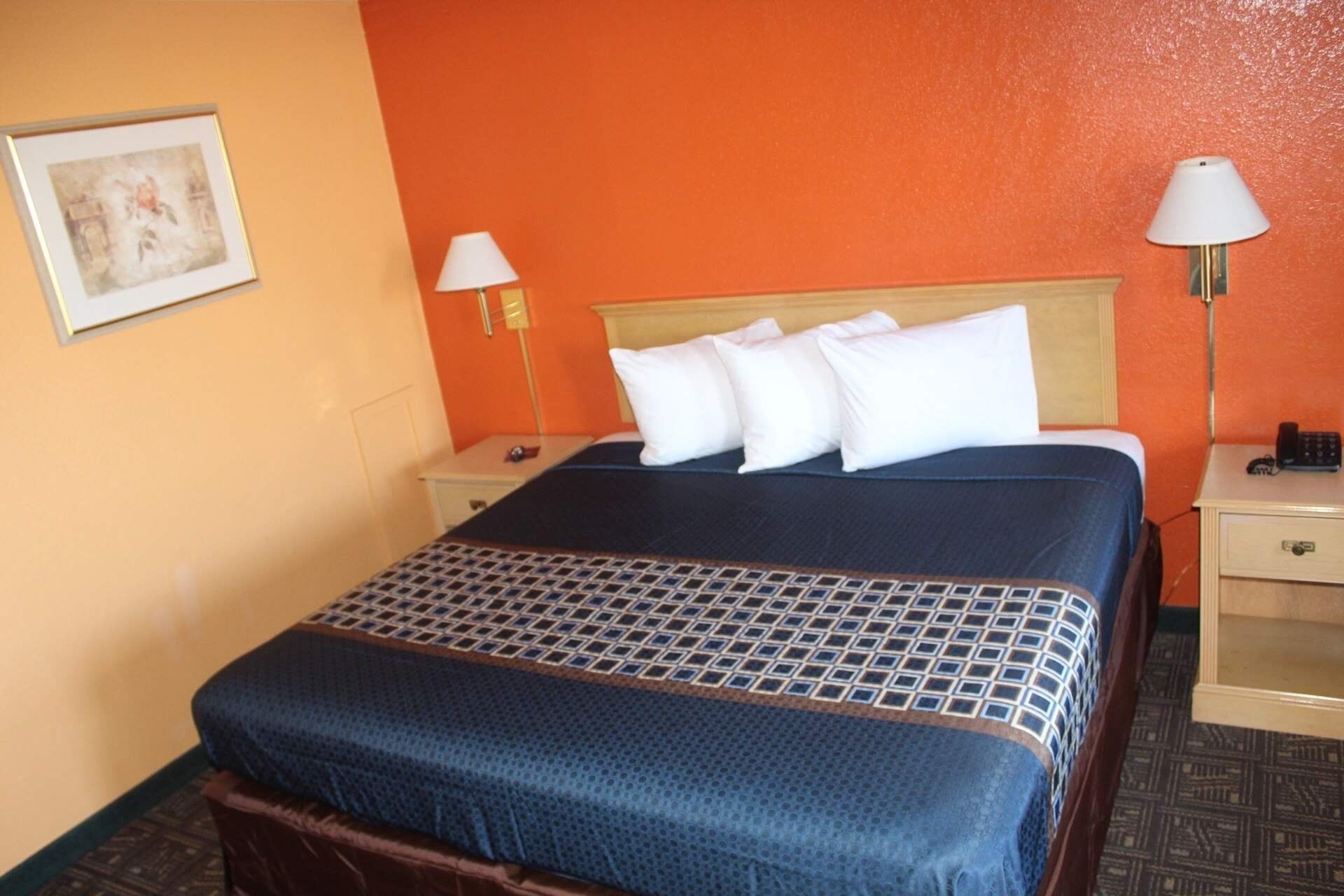A hotel room with a bed, two bedside tables, a lamp, and a painting on the wall.