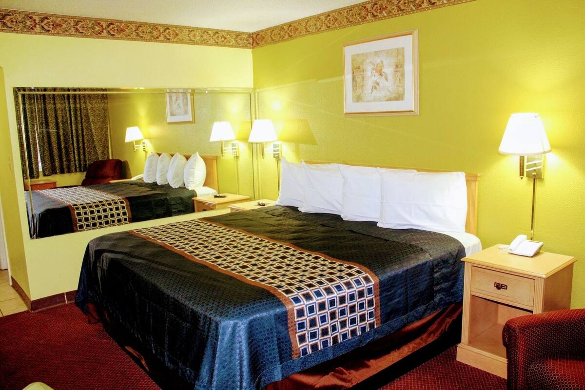 A hotel room with a large bed, two bedside tables, a chair, a mirror, and a framed picture on the wall.