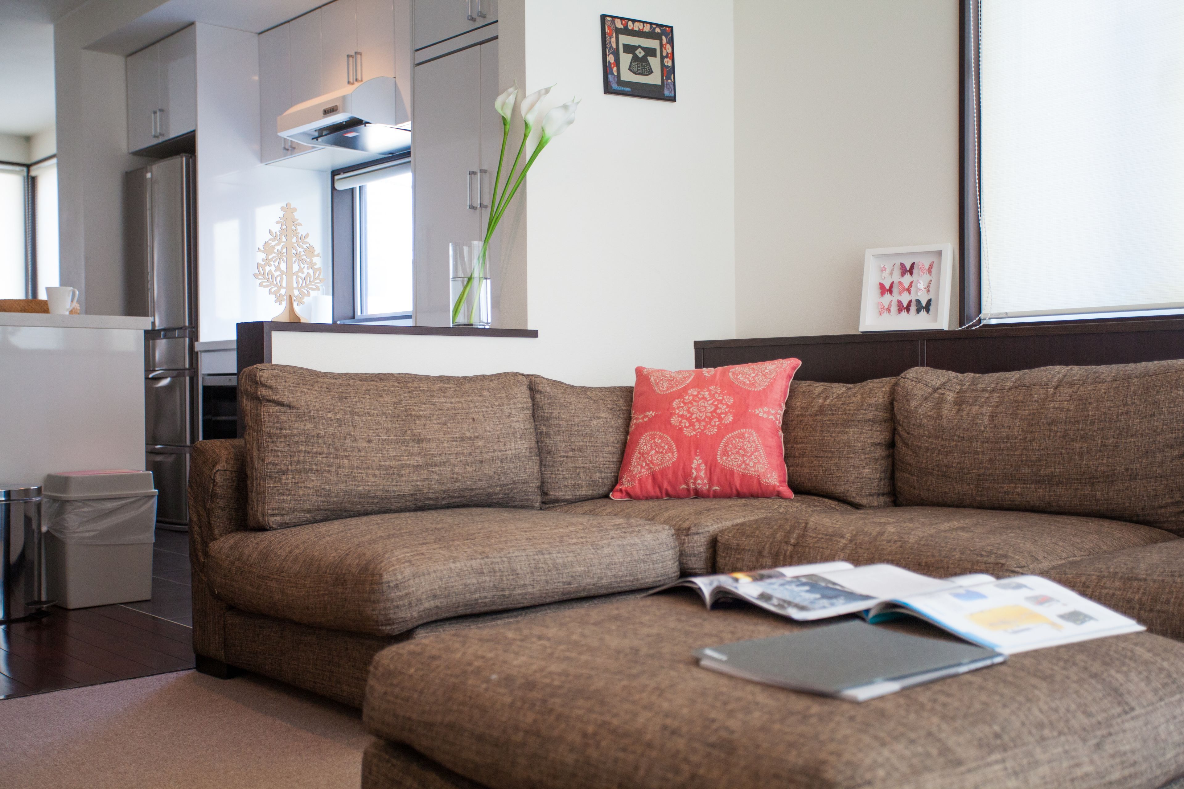 Un salon moderne avec un canapé d’angle marron, un coussin rouge à motifs et un magazine posé sur le canapé.