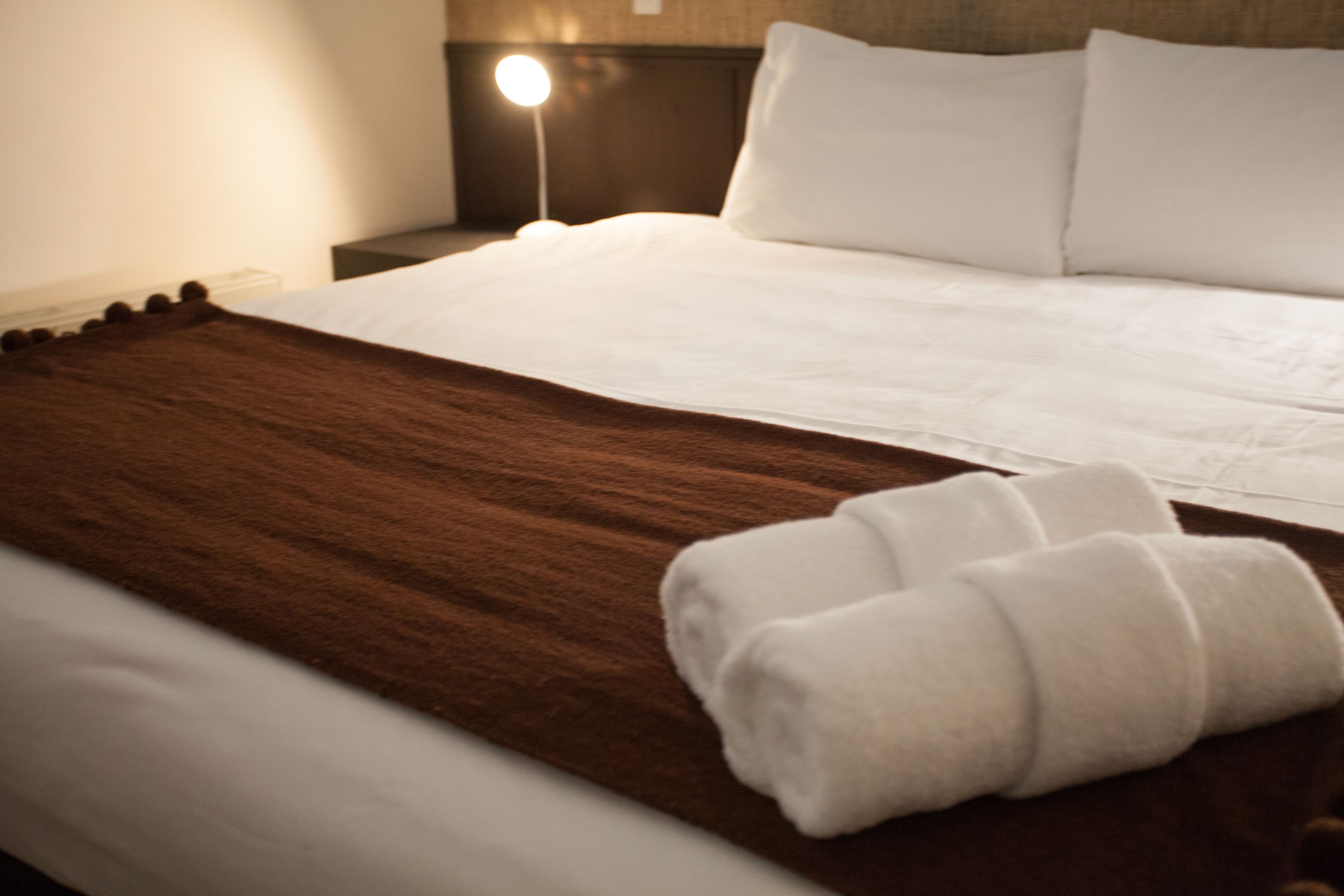 A neatly made bed with white linens and a brown throw blanket.