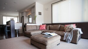 A modern living room with a sectional sofa, a coffee table, and a large window. - Neyuki (Kutchan)