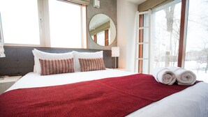 A hotel room with a large bed, a red throw blanket, and a view of the outdoors. - Yume Basho (Kutchan)