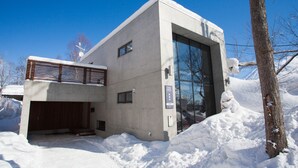 A modern building with a large glass window, a wooden slatted roof, and a snow-covered ground. - Yume Basho (Kutchan)
