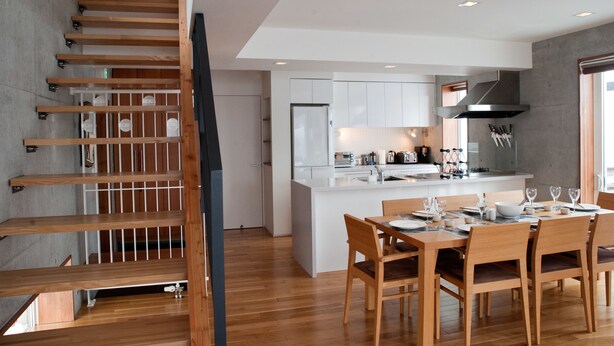 A modern kitchen with white cabinetry, a central island, and a dining area with wooden furniture. - Yume Basho (Kutchan)