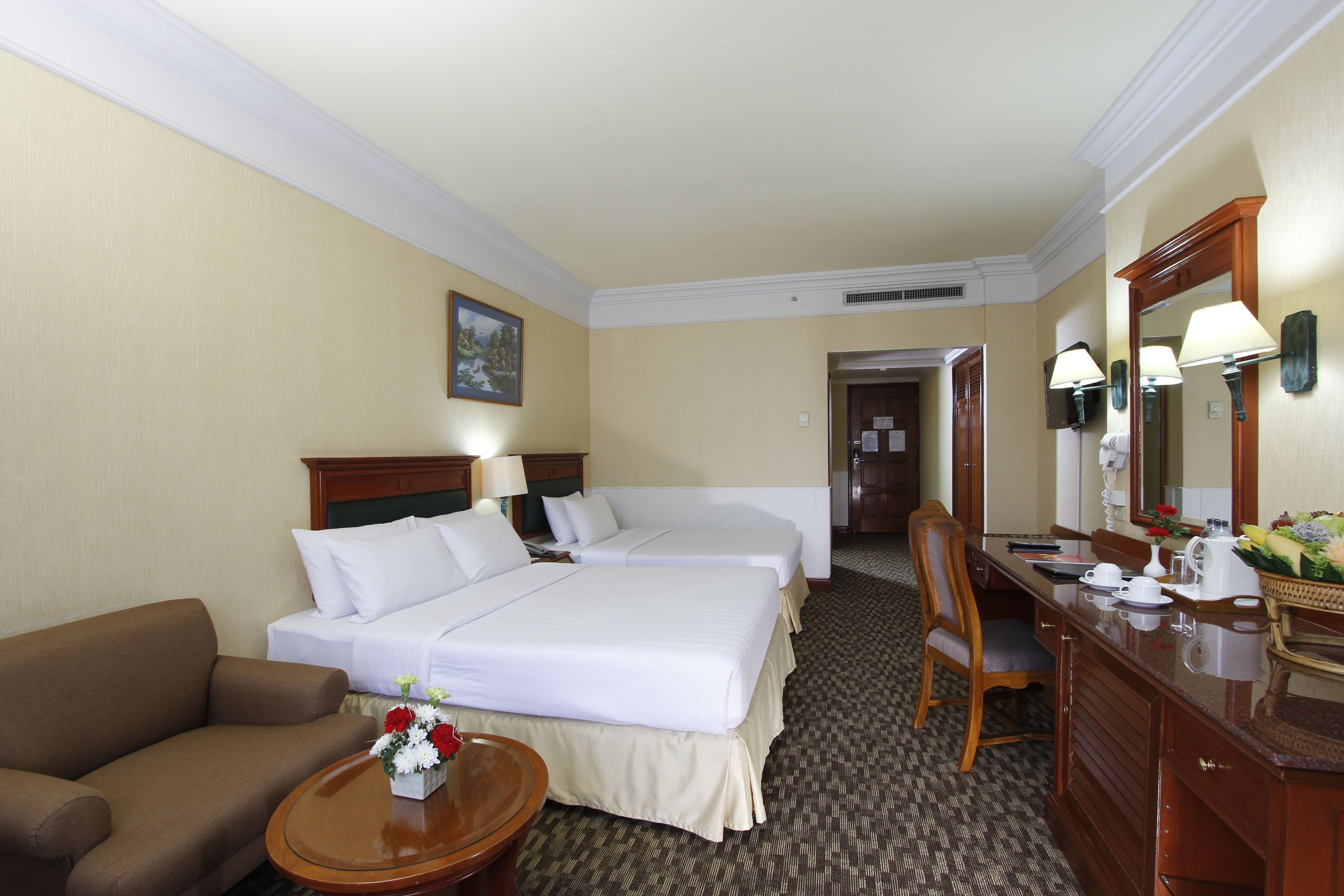 A hotel room with two beds, a sofa, a desk, and a mirror.