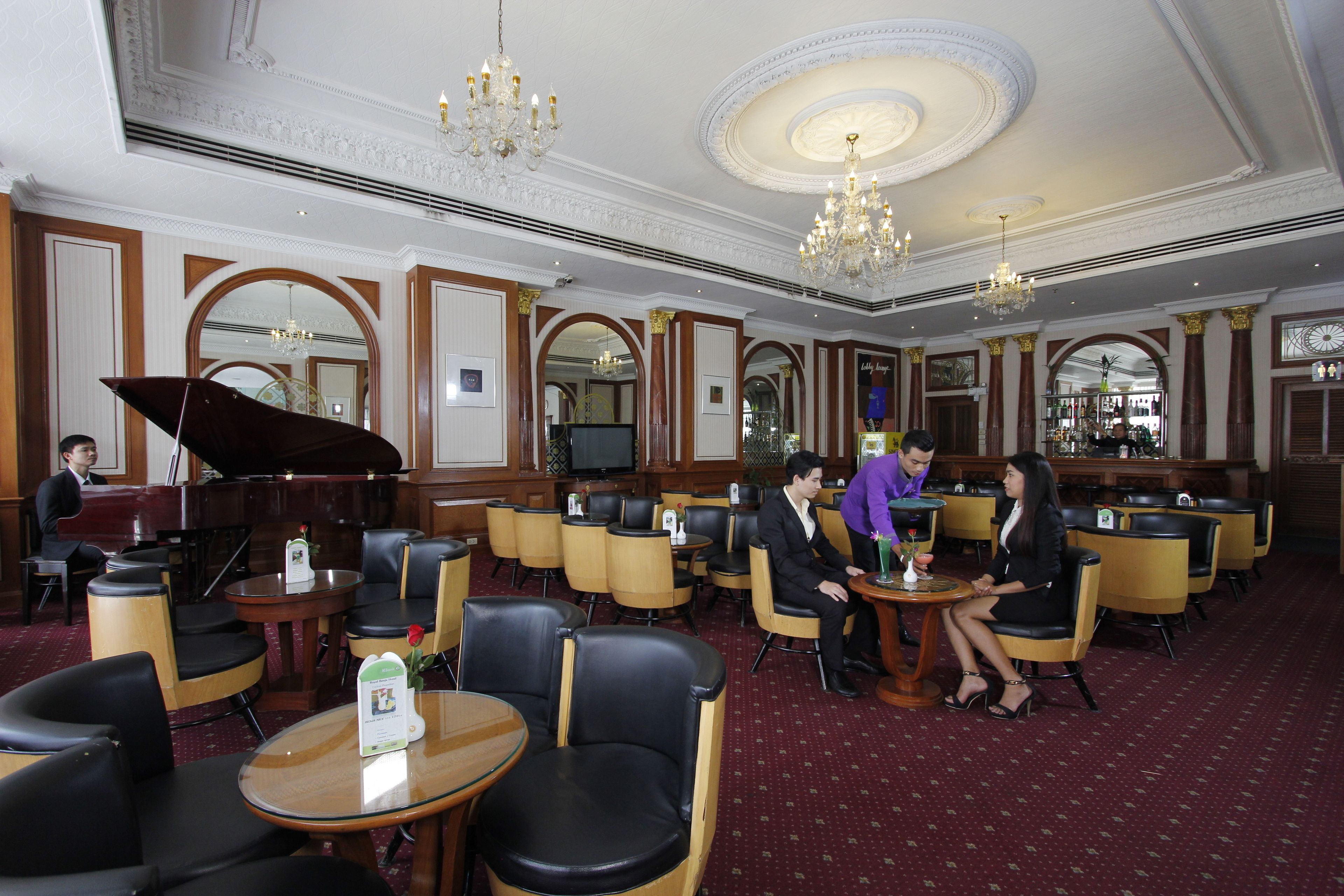 A hotel lobby with a grand piano, multiple seating areas, and chandeliers.
