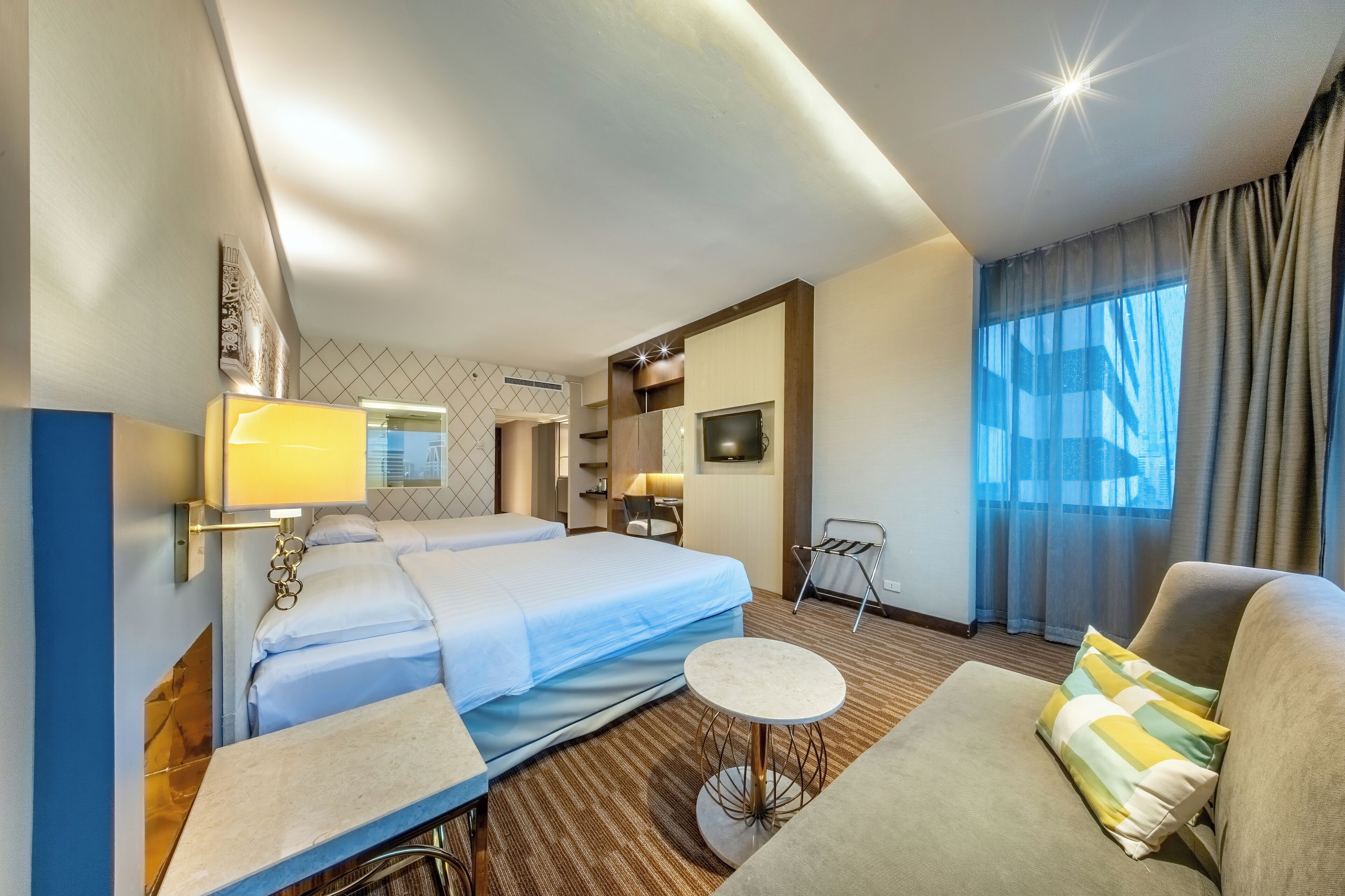 A hotel room with two beds, a sofa, a small round table, a TV, and a window with curtains.