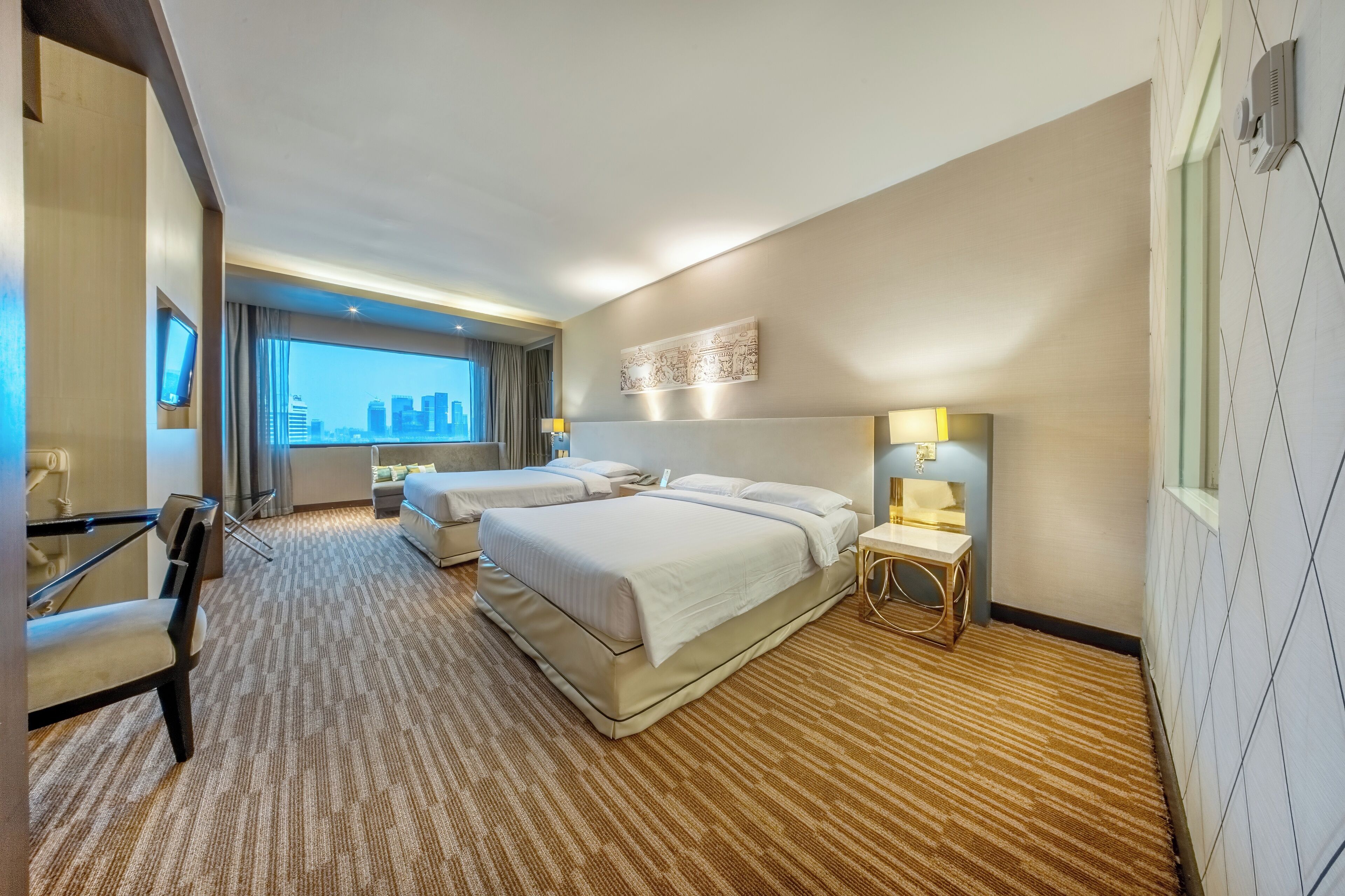 A hotel room with two beds, a desk, a chair, a city view, and a wall-mounted artwork.