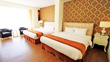 A hotel room with two beds, a sofa, a nightstand, and a patterned wallpaper.