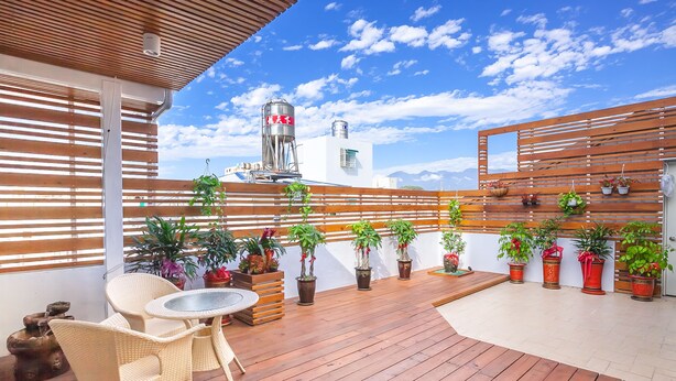 Una terraza de madera con plantas en macetas, sillas de mimbre y una mesa.