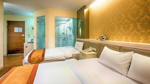 Habitación de hotel con dos camas, zona de ducha, teléfono junto a la cama y un espejo.