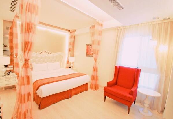 Une chambre d’hôtel avec un grand lit, un fauteuil rouge, une petite table et des rideaux légers.