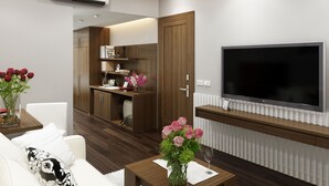 A modern living room with a flat-screen TV, a sofa, a coffee table, and a kitchen area with wooden cabinets and a built-in oven. -  Eco Luxury Hotel Hanoi (Hanoi)