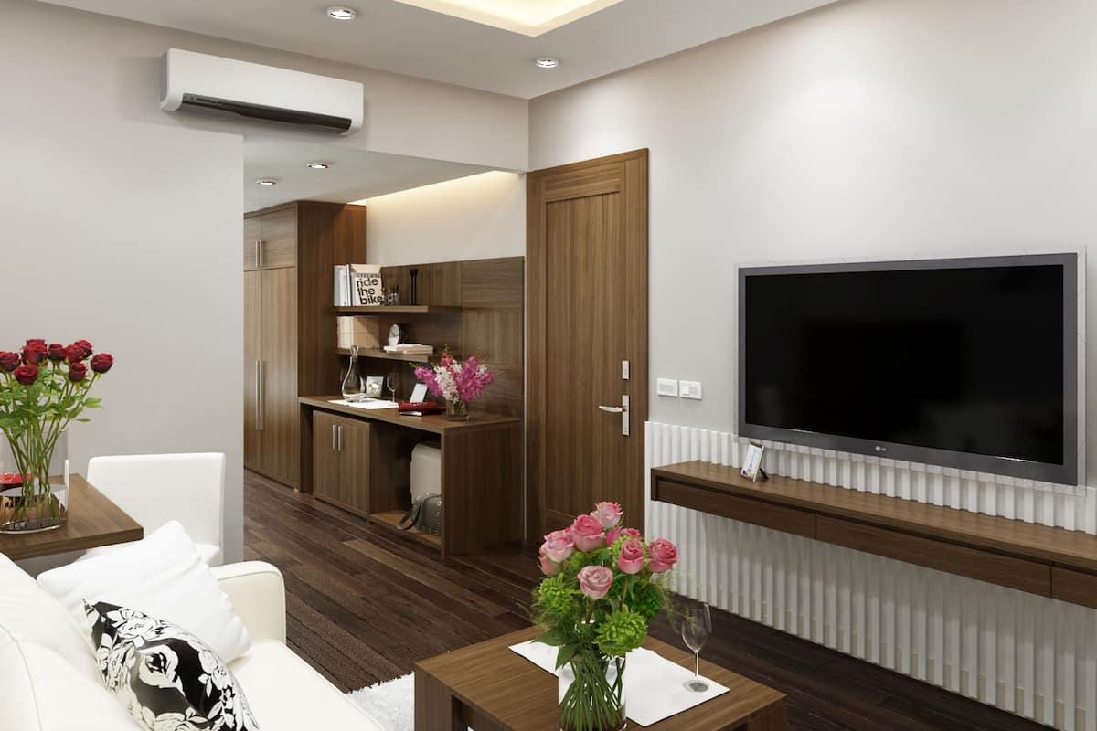 A modern living room with a flat-screen TV, a sofa, a coffee table, and a kitchen area with wooden cabinets and a built-in oven.