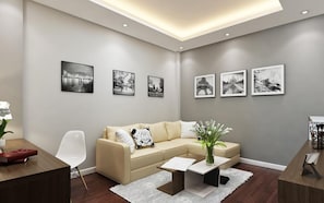 A modern living room with a beige sectional sofa, a white coffee table, and a small side table. There are six black-and-white photographs on the wall. -  Eco Luxury Hotel Hanoi (Hanoi)
