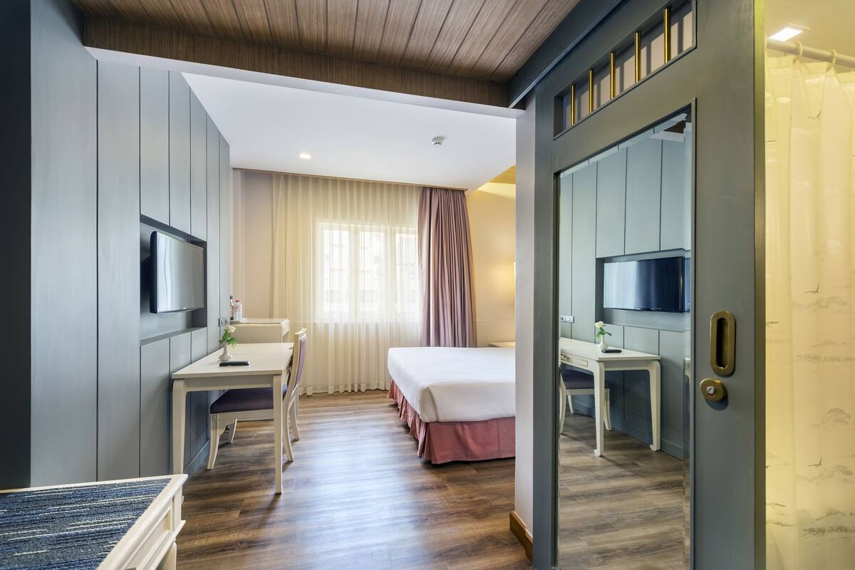 Ein Hotelzimmer mit Bett, Schreibtisch, Stuhl, Fernseher und einer Tür mit Spiegel.