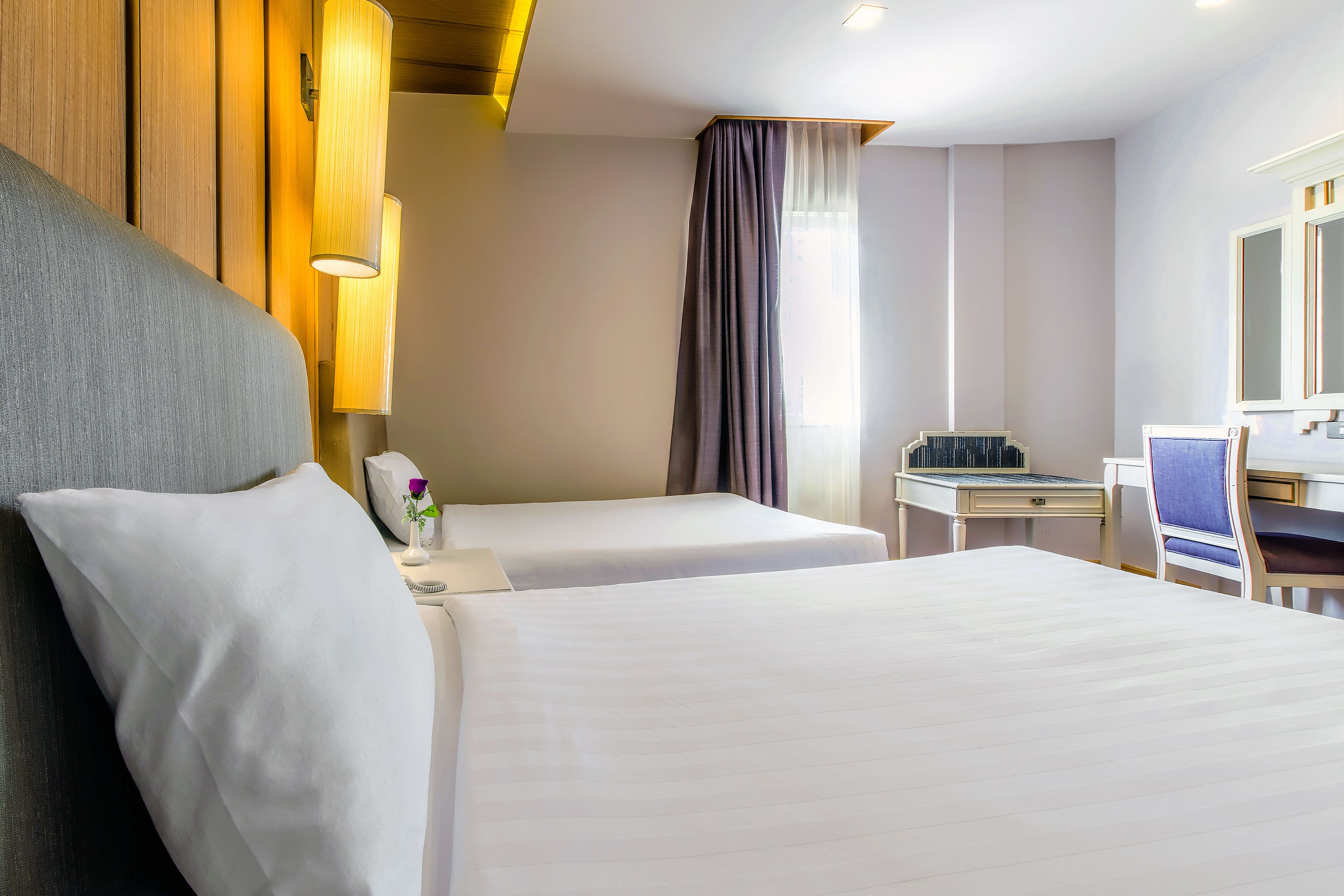 Una camera d'albergo con due letti, una scrivania, una sedia e uno specchio grande.