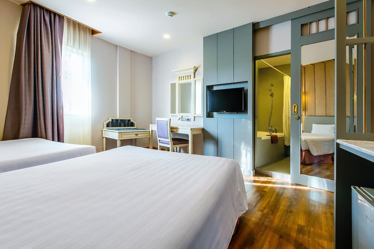 Ein Hotelzimmer mit zwei Betten, einem Schreibtisch, einem Fernseher und einem durchgegangenen Badezimmer.